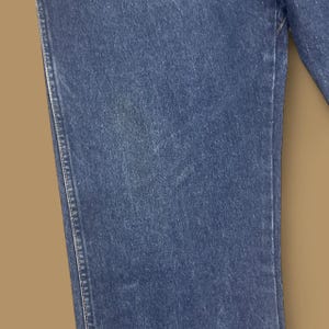 K&ouml;nnte beinhalten: Nahaufnahme eines Abschnitts blauer Jeans. Der Stoff zeigt eine strukturierte Oberfl&auml;che mit sichtbaren N&auml;hten entlang der N&auml;hte. Der Denim hat eine klassische, mittelblaue Waschung.