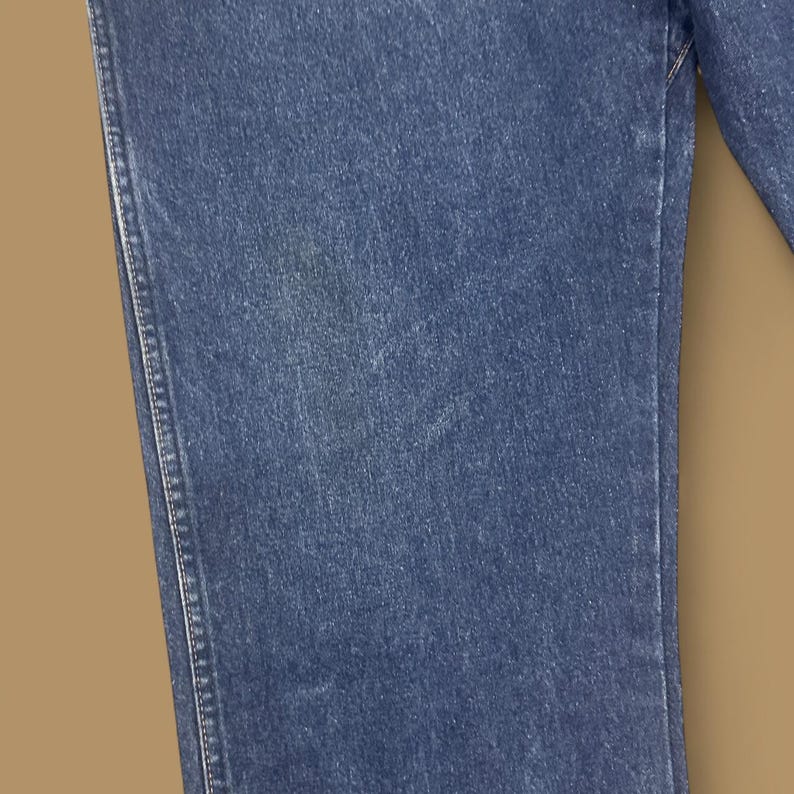 K&ouml;nnte beinhalten: Nahaufnahme eines Abschnitts blauer Jeans. Der Stoff zeigt eine strukturierte Oberfl&auml;che mit sichtbaren N&auml;hten entlang der N&auml;hte. Der Denim hat eine klassische, mittelblaue Waschung.
