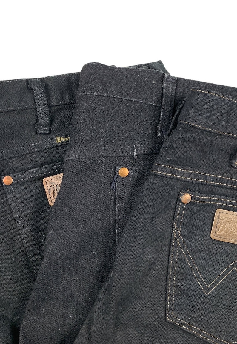 May include: Two pairs of black denim jeans with a brown leather patch on the back pocket that says "Wrangler".