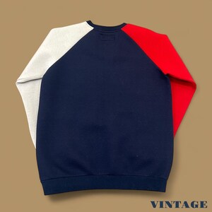 May include: A vintage crew neck sweatshirt with a color block design. The sweatshirt features a navy blue body, a red right sleeve, and a light gray left sleeve. The word "VINTAGE" is printed in white at the bottom.