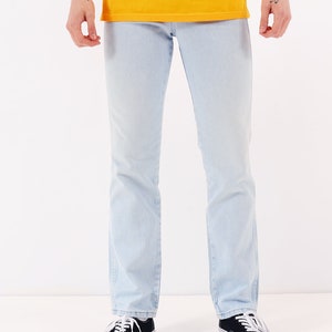 May include: A person wearing light blue jeans and black sneakers. The jeans have a straight leg fit.