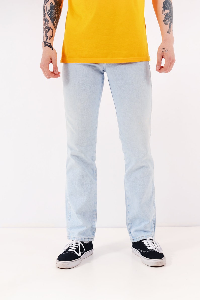 May include: A person wearing light blue jeans and black sneakers. The jeans have a straight leg fit.
