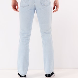 May include: A pair of light blue denim jeans with a brown leather patch on the back pocket that says "Wrangler".