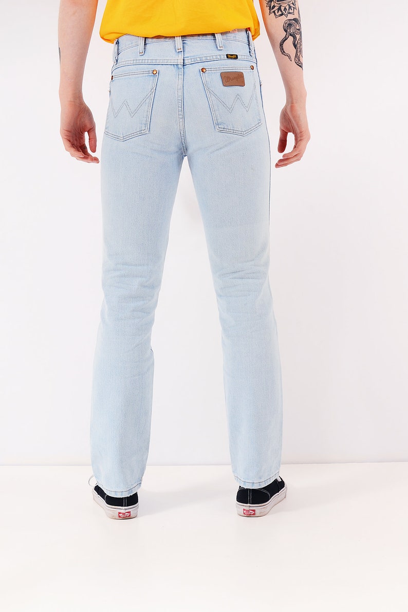 May include: A pair of light blue denim jeans with a brown leather patch on the back pocket that says "Wrangler".