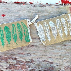 Op de afbeelding: Twee jute zakjes met ritsen. Eén zakje heeft een groen verenpatroon en het andere een wit verenpatroon.