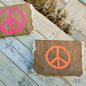 Op de afbeelding: Twee jute zakjes met peace-teken ontwerpen. Het bovenste zakje heeft een felroze peace-teken en het onderste zakje heeft een oranje peace-teken.