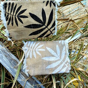 Op de afbeelding: Twee jute zakjes met rafelige randen, een met zwarte bladmotieven en de andere met witte bladmotieven.