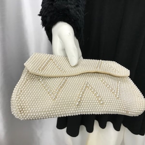 May include: A white beaded clutch bag with a geometric pattern. The bag is made of small, round pearls.