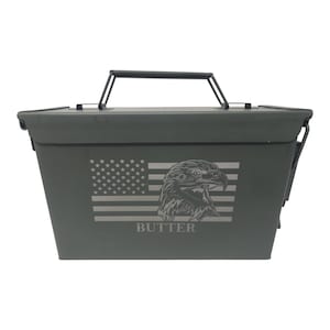 May include: A green metal ammo can with a black handle. The can has an American flag and an eagle engraved on the front. The name "BUTTER" is engraved below the eagle.
