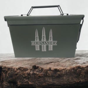 May include: A green metal ammo can with a black handle. The can has a personalized inscription that reads "HERNANDEZ" with three bullet silhouettes above the name.