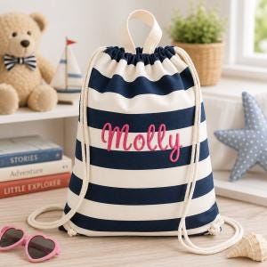 May include: A drawstring backpack featuring horizontal navy blue and white stripes. The bag has a top handle and thick white rope straps. The name Molly is embroidered in pink cursive script across the centre of the front of the fabric bag.
