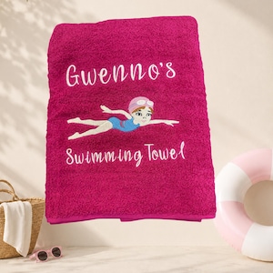 May include: A magenta swimming towel with the name "Gwenno's" embroidered in white script. The towel features an embroidered illustration of a swimmer and the words "Swimming Towel".