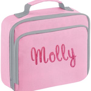 Puede incluir: Una bolsa de almuerzo rectangular de color rosa con ribetes grises y un asa superior. La parte frontal presenta el nombre Molly bordado en una letra cursiva de color rosa oscuro. La bolsa incluye un compartimento frontal y cierre con cremallera.