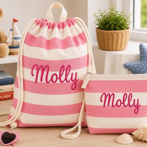 May include: A pink and white striped drawstring backpack and a matching zippered pouch, both featuring the name Molly embroidered in pink script. The items are made of fabric and include thick white rope cords for the backpack closure.