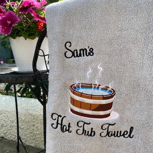 May include: A gray bath towel with black embroidery that says "Sam's Hot Tub Towel" and a cartoon image of a hot tub with steam rising from it.