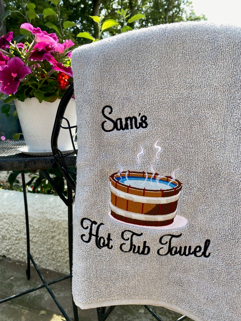 May include: A gray bath towel with black embroidery that says "Sam's Hot Tub Towel" and a cartoon image of a hot tub with steam rising from it.