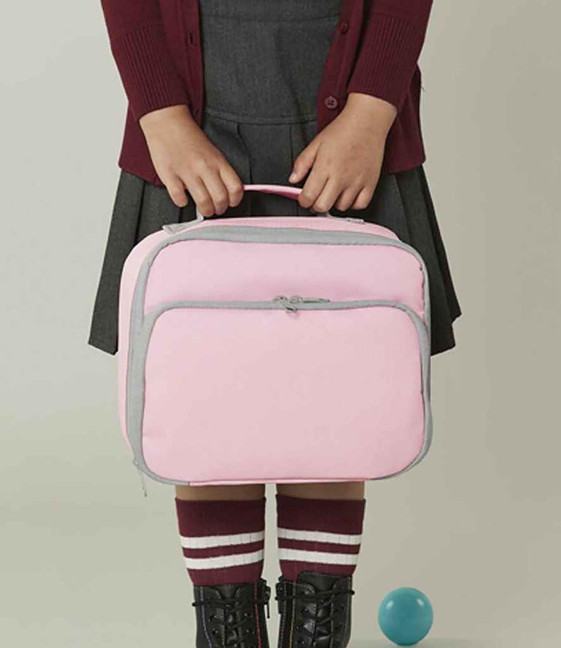 Puede incluir: Una bolsa de almuerzo rectangular en un suave color rosa pastel con cierre de cremallera gris y ribete gris en los bordes. La bolsa incluye un asa superior para transportarla y un bolsillo frontal grande con cremallera, ofreciendo un dise&ntilde;o estructurado.