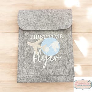 May include: Grey felt pouch with a white embroidered design of a plane flying over a globe with the text "First Time Flyer".