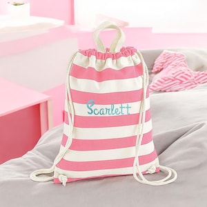 Può includere: Uno zaino con chiusura a coulisse a righe orizzontali rosa e bianche. La borsa è dotata di una maniglia superiore e di spallacci in corda bianca. Il nome Scarlett è ricamato in corsivo azzurro al centro del pannello frontale.