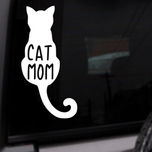 May include: White vinyl decal of a cat silhouette with the text "CAT MOM" on a black car window.