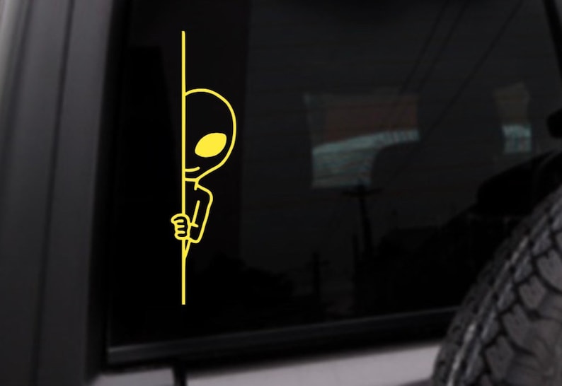 May include: A yellow alien sticker peeking around a corner. The alien has a large head, small body, and a big smile.