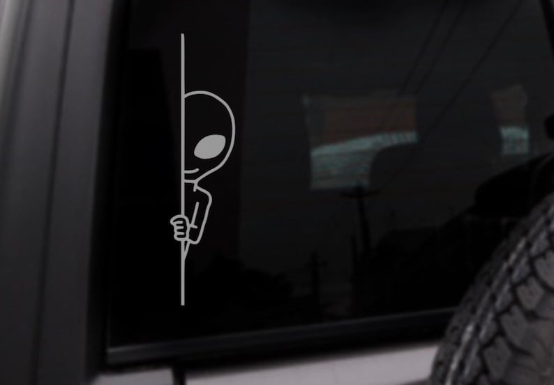 May include: A black and white sticker of an alien peeking around a corner. The alien is drawn in a simple cartoon style.