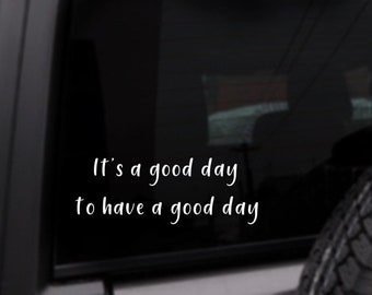 May include: A black car window with a white vinyl decal that reads "It's a good day to have a good day".