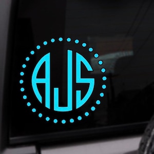 May include: A blue monogram decal with the letters AJS in a circle with a dotted border. The decal is on a black background.