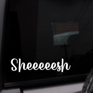 May include: A white vinyl sticker with the word "Sheeeeesh" written in a cursive font on a black car window.