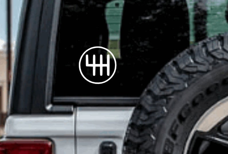 May include: A white vinyl sticker with a black outline of a 4-speed manual transmission gear shift pattern. The sticker is on the back window of a silver car.