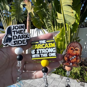 May include: Three retractable badge reels with Star Wars-themed designs. One features Darth Vader with the text "Join the Dark Side." Another says "The Sarcasm is Strong with This One." The third depicts Chewbacca.