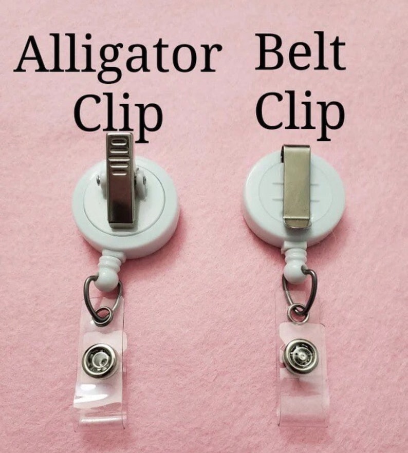 May include: Two white badge reels with different metal clips. The left reel has an alligator clip, and the right reel has a belt clip. Both reels have a clear plastic strap with a snap closure and a metal ring.
