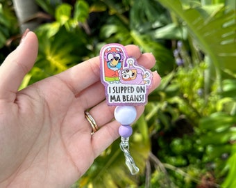 May include: A purple and pink glitter badge holder with a cartoon image of two characters. The text on the badge holder reads "I slipped on ma beans!"