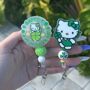 May include: Two Hello Kitty themed retractable badge holders. One features a green shamrock with the text "Happy St. Patrick's Day" and the other features Hello Kitty holding a green shamrock. Both have green, white, and rainbow beads.