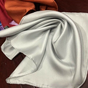 May include: A light gray silk scarf folded in a triangle shape. The scarf is smooth and has a subtle sheen.