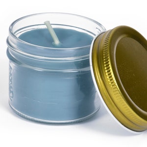 May include: A blue candle in a clear glass jar with a gold lid. The candle has a white wick.
