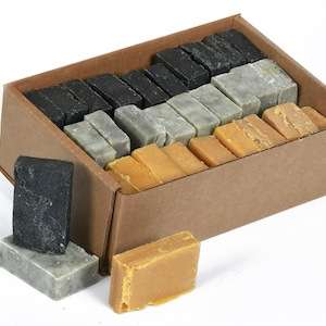 May include: A cardboard box filled with bars of soap in three colors: black, gray, and yellow. The box is open and some bars of soap are spilling out.