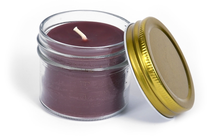 May include: A glass jar candle with a purple wax and a white wick. The jar has a gold lid.