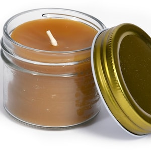 May include: A small glass jar candle with brown wax and a white wick. The jar has a gold metal lid.