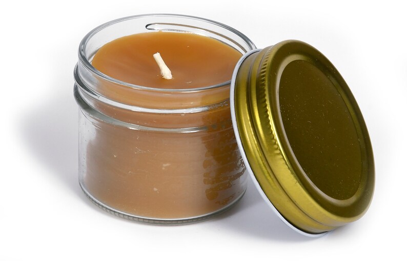 May include: A small glass jar candle with brown wax and a white wick. The jar has a gold metal lid.
