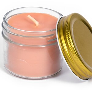 May include: A glass jar candle with pink wax and a gold lid. The candle has a single wick.