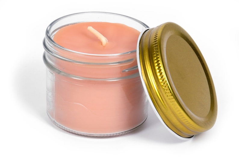May include: A glass jar candle with pink wax and a gold lid. The candle has a single wick.