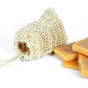 May include: A natural loofah soap bag with a drawstring closure, next to a stack of four rectangular bars of natural soap.