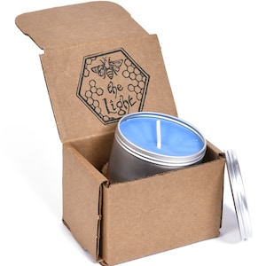 May include: A blue candle in a silver tin with a cardboard box. The box is open and the candle is inside. The box has a logo that says "the light" with a bee and honeycomb design.