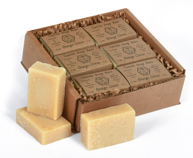May include: A box of eight bars of orange citrus Castile soap. The soap bars are packaged in a brown cardboard box with shredded paper inside. The soap bars are individually wrapped in paper and have a label that says "Castile Soap Bars" and "Orange Citrus".