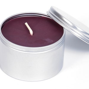 May include: A silver tin candle with a purple wax and a white wick. The lid is off and the candle is sitting on a white surface.