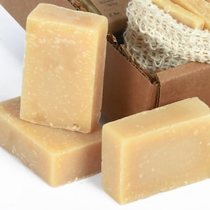 May include: Three bars of natural soap in a cardboard box. The soap is a light beige color and has a rough texture.
