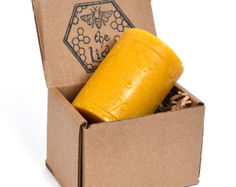 May include: A yellow beeswax candle with a honeycomb and bee design is in a brown cardboard box with the words "the little" printed on the side.