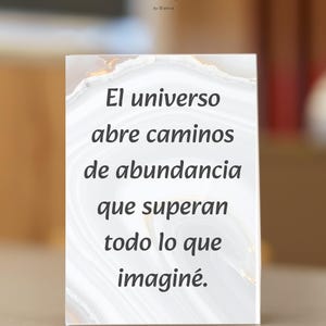 Puede incluir: Un letrero rectangular blanco con el texto "El universo abre caminos de abundancia que superan todo lo que imaginé." El letrero tiene un borde tipo mármol y el logo "My Inner Self".