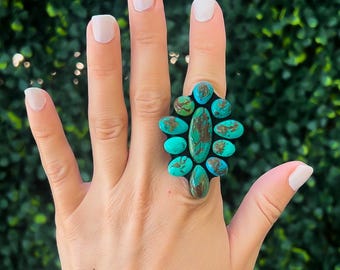 May include: A large statement ring featuring turquoise and brown oval-shaped stones. The ring's design is set against a green background. The ring is a bold piece of jewelry.